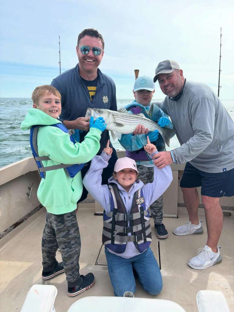 Two dads and three kids holding up a striped bass aboard the charter boat