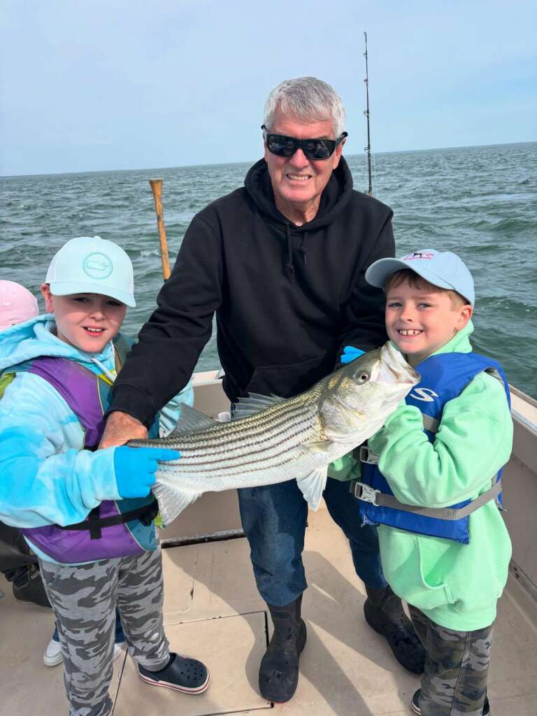 The boat captain and two young anglers holding a striped bass together