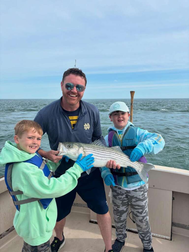 A dad and two kids proudly holding their striped bass catch