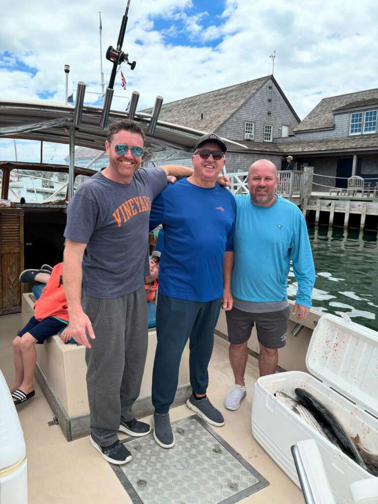 Three anglers back at the dock with a cooler of striped bass after the trip