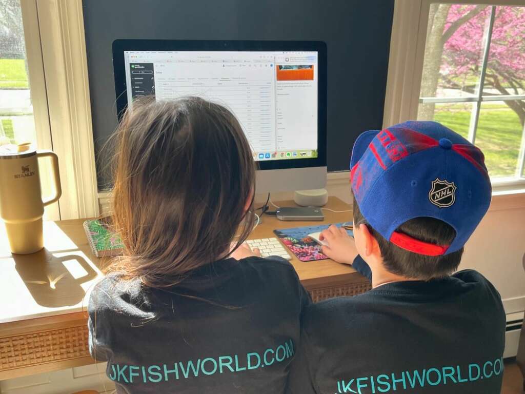 Two kids in JK-Fish shirts working at the computer, learning the business